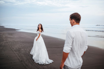 Fototapeta na wymiar Elegant gorgeous bride and groom walking on ocean beach during sunset time. Romantic walk newlyweds on tropical island. Concept marriage, just married