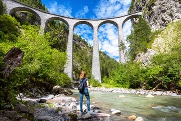 Papier Peint photo Viaduc de Landwasser Viaduc de Landwasser à Filisur, Suisse. Jeune femme regarde la célèbre attraction touristique. Panorama pittoresque du pont ferroviaire élevé dans les montagnes. Une fille adulte voyage dans les Alpes suisses en été.