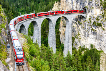 Landwasserviadukt in Filisur, Schweiz. Es ist berühmtes Wahrzeichen der Schweiz. Roter Schnellzug auf hoher Brücke in den Bergen. Malerischer Blick auf die erstaunliche Eisenbahn im Sommer. Konzept des Reisens in Alpeneuropa.