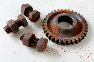 Rusty bolts, nuts and gear wheel made of chocolate on white background. Chocolate chip scattered on smooth surface. Mechanic gearing background. Father's day card obects