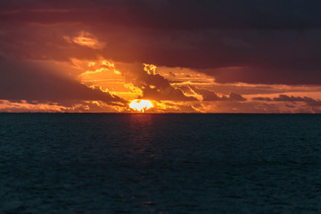 Obraz premium Pacific Ocean, French Polynesia, Society Islands, Leeward Islands, Bora Bora. View of sun setting over ocean creating a bright orange sky.