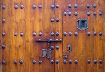 Locked up old decorative wooden door with a small peeping window.