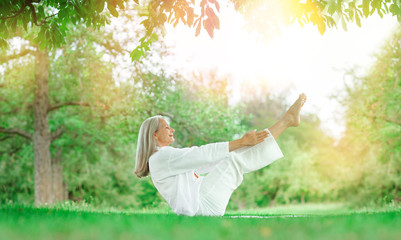 beautiful best age Senior woman with long grey hair doing yoga exercises outdoors