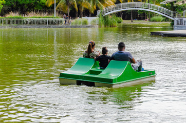 family sailing in pedal boat on a lake surrounded by natural and tropical landscapes of a park