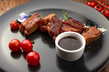Fried ribs on a black plate with sauce and tomatoes