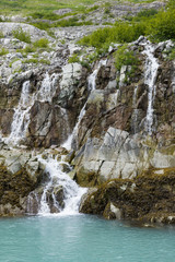 Alaska, Glacier Bay National Park. A fresh waterfall cascades down rocky cliffs to the sea in Muir Inlet.
