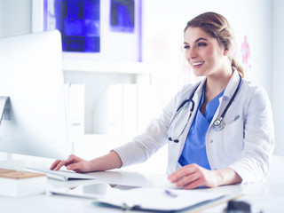 Young female doctor sitting at a desk and working on the computer at the hospital office. Health care, insurance and help concept. Physician ready to examine patient