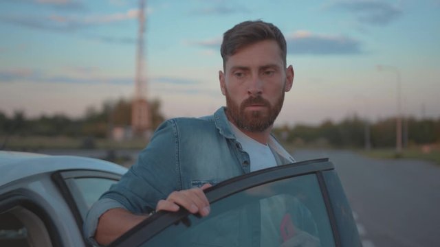 Young male driver gets out of car and looks on breakdown autonmobile on the road. Shocked stressed young man calling for emergency services in car trouble.