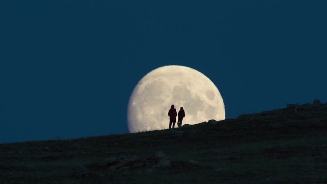 Silhouette of woman and child standing against huge moon background.