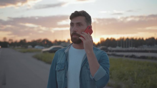 Portrait of stressed male driver talking by cellphone with car services explaining the situation car accident breakdown on countryside road.