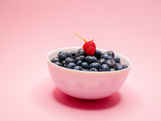 Blueberries on a plate. on a guards, pink background. from the top is a raspberry berry. concept of vitamins, berries. Breakfast ripe, large blueberries. Horizontal. side view