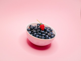 Blueberries on a plate. on a guards, pink background. from the top is a raspberry berry. concept of vitamins, berries. Breakfast ripe, large blueberries. Horizontal. side view