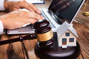 House Model With Gavel In Front Of Businessperson Using Laptop