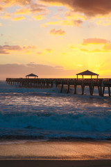Fototapeta premium Juno Beach, Florida. Golden sunrise and crashing waves over the pier at Juno Beach