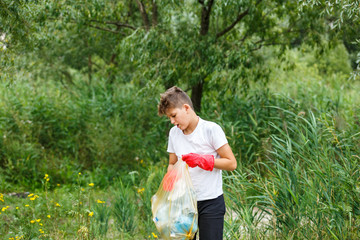 Boy in white t shirt in gloves collects garbage and plastic bottles into blue package on the beach. Young volunteer. Environmental protection, save environment concept