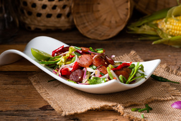 Spicy Chinese pork sausage with vegetable Thai salad in white plate on wood background