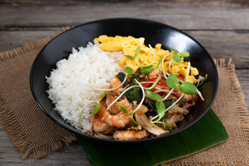 Rice topped with stir-fried shrimp and basil, and fried eggs in white dish.