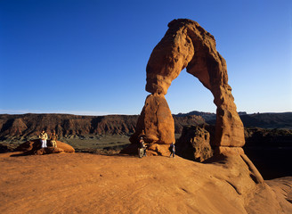 Hikers pause for a rest at Utah's iconic Delicate Arch, Arches NP.