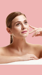 Portrait of pretty woman with smooth soft skin touching cheek on pink background, aspect ratio and...
