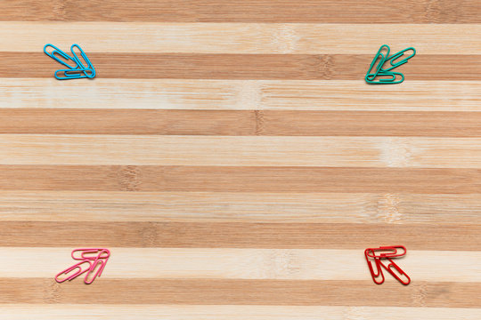 Four paperclips of different colors all pointing towards the center on a table , shot from above, arranged in all corners.