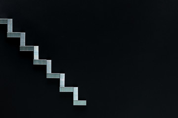 A graph going downwards made with staples on a black background , shot from above.