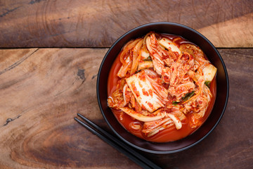 Kimchi cabbage in a bowl with chopsticks on wooden background, Korean food