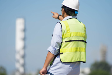 rear view of male engineer walking and pointing on bright blue sky for planing a construction dress with protective vest, hard helmet