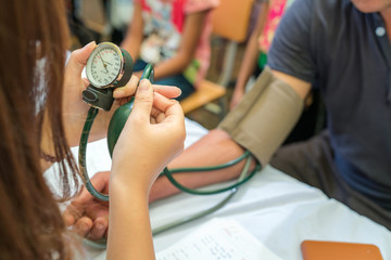 Volunteer nurse measuring blood pressure of poor Asian people outdoors closeup