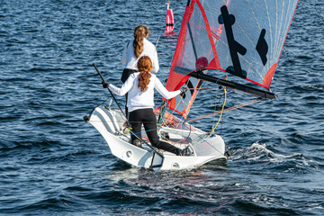 Naklejka premium Two Girls Sailing small sailboat with long red hair viewed closeup from behind.
