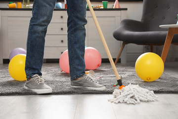 Man with mop cleaning messy room after party, closeup view of legs