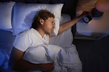 Sleepy young man turning off alarm clock on nightstand, view from above. Bedtime