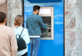 Young people standing in queue to cash machine outdoors
