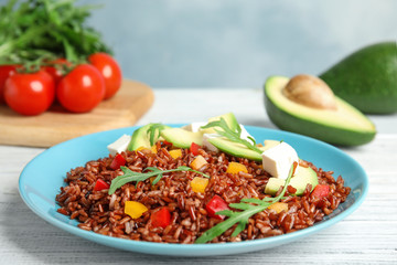 Plate with delicious cooked brown rice on white wooden table