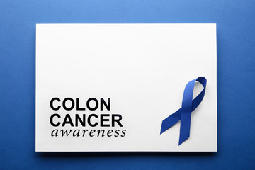 Card with words COLON CANCER AWARENESS and blue ribbon on color background, top view. Space for text