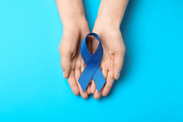 Woman holding blue awareness ribbon on color background, top view. Symbol of social and medical...