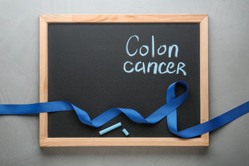Chalkboard with blue awareness ribbon and words COLON CANCER on grey background, top view. Space...