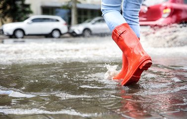 Woman with rubber boots running in puddle, closeup. Rainy weather