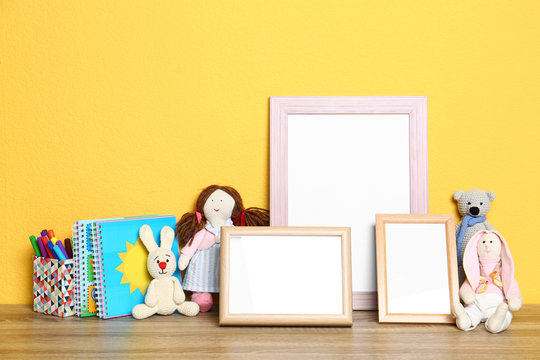 Soft toys and photo frames on table against yellow background, space for text. Child room interior