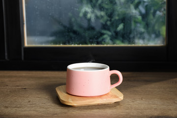 Cup of hot drink on window sill against glass with rain drops, space for text