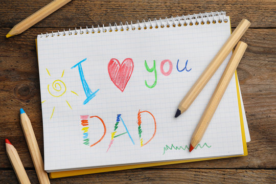 Notebook with words I LOVE YOU DAD and pencils on wooden table, flat lay
