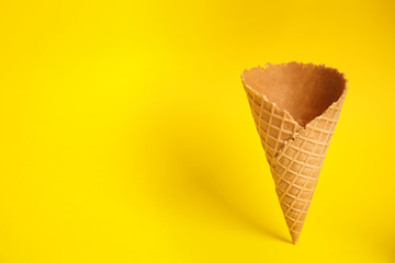 Empty wafer ice cream cone on yellow background. Space for text