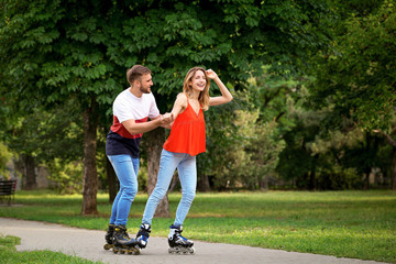 Young happy couple roller skating in summer park