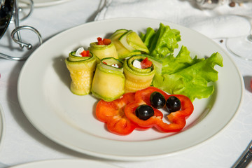 A restaurant dish of stuffed zucchini and sweet pepper on a table in a plate. Cold appetizer.