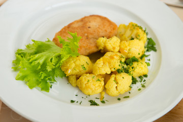 A dish of fried chicken cutlet and boiled cauliflower in a plate in the interior of the restaurant.