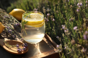 Glass of fresh lemonade on wooden tray in lavender field. Space for text