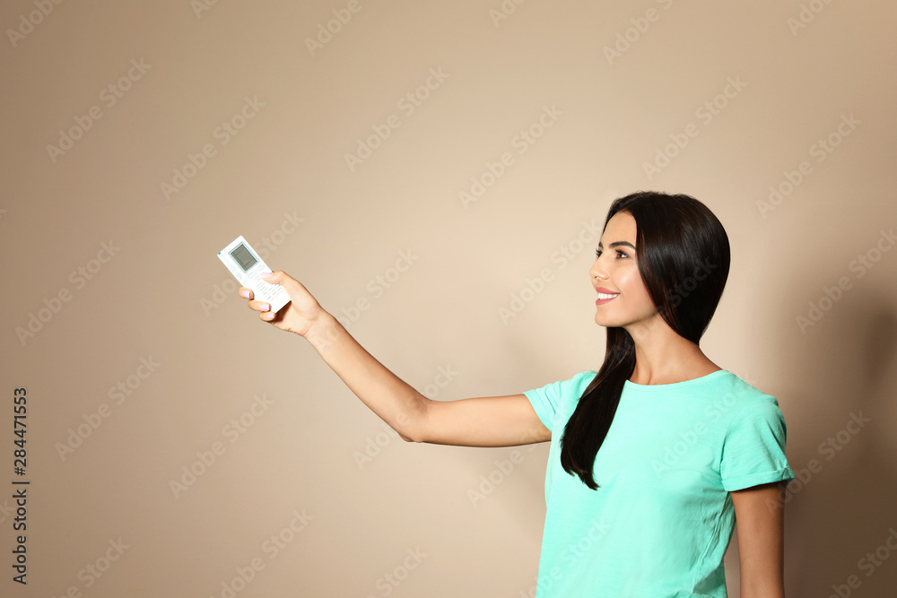 Canvas Prints young woman with air conditioner remote on beige background. space for text