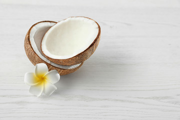Halves of coconut and flower on white wooden background. Space for text