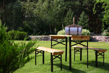 Picnic basket with blanket on wooden table in green park