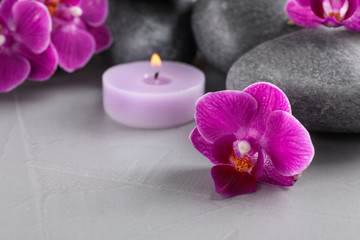 Spa stones, orchid flowers and candle on grey table, closeup