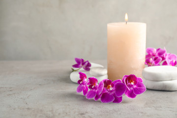 Orchid flowers, spa stones and candle on grey table. Space for text